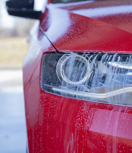 Car wash close-up. Washing a modern car with high-pressure water and soap, cleaning the headlights