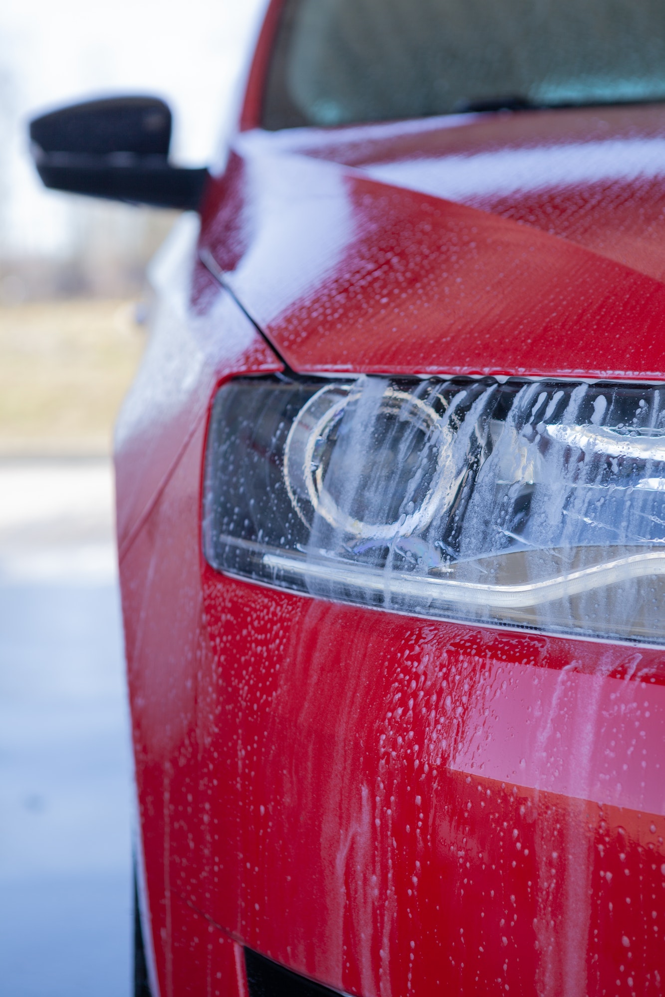 Car wash close-up. Washing a modern car with high-pressure water and soap, cleaning the headlights
